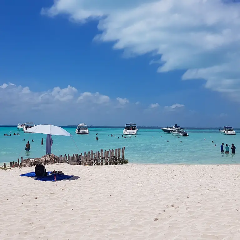 Weißer Sandstrand an der Playa Centro auf Isla Mujeres mit Sonnenschirm und Booten im türkisfarbenen Karibischen Meer