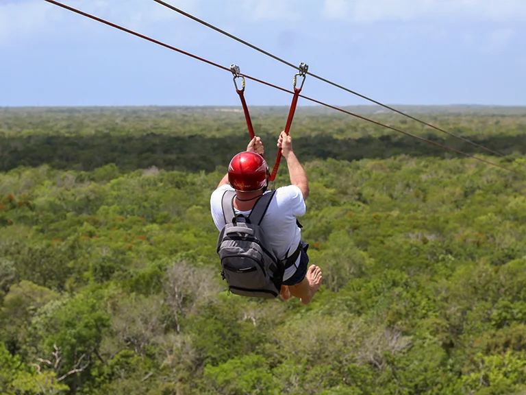 Person fährt bei einer Zipline-Tour über den grünen Dschungel der Riviera Maya.