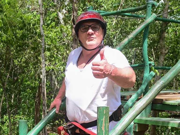 Teilnehmer mit Helm und Klettergurt gibt nach dem Zipline-Abenteuer in der Riviera Maya den Daumen hoch.
